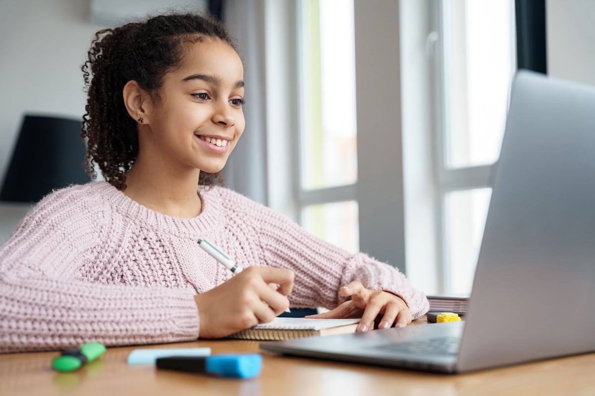 Young teen student studying online with online teacher on laptop at home.